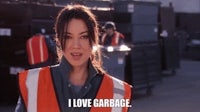 a woman in an orange vest standing next to a pile of garbage